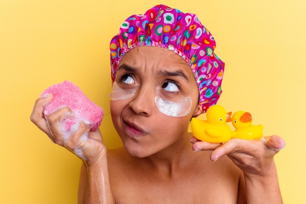 Jovem mestiça tomando banho segurando uma esponja e patos de borracha