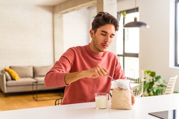 Jovem mestiço comendo aveia e leite no café da manhã em sua cozinha