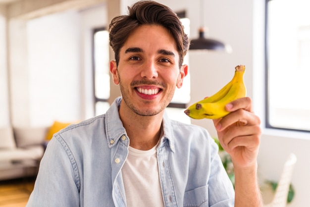 Foto jovem mestiço comendo banana na cozinha de sua casa