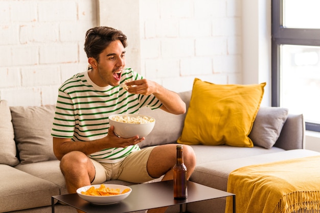 Jovem mestiço comendo pipoca sentado no sofá