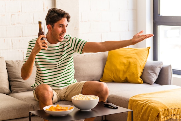 Foto jovem mestiço comendo pipoca sentado no sofá