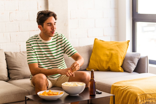 Jovem mestiço comendo pipoca sentado no sofá