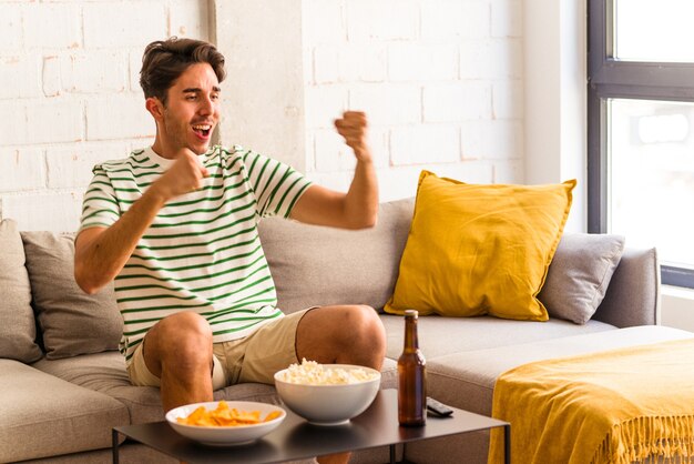 Jovem mestiço comendo pipoca sentado no sofá