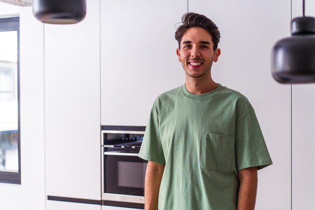 Jovem mestiço em sua cozinha feliz, sorridente e alegre.