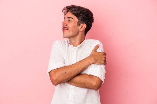 Jovem mestiço isolado em um fundo branco abraços, sorrindo despreocupado e feliz.