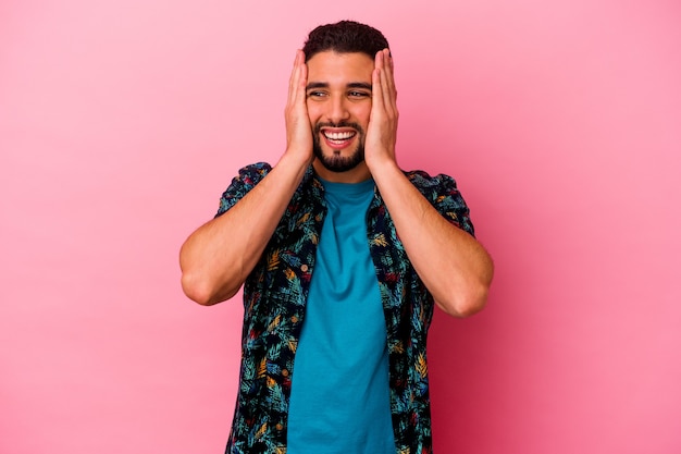 Jovem mestiço isolado em um fundo rosa, cobrindo as orelhas com as mãos, tentando não ouvir o som muito alto.