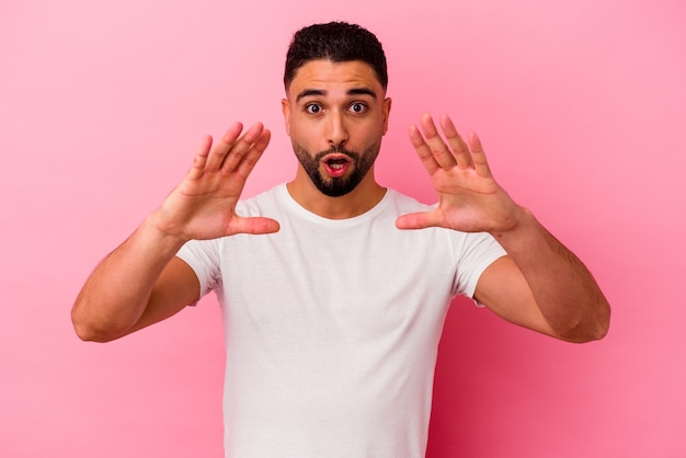 Jovem mestiço isolado em um fundo rosa, comemorando uma vitória ou sucesso, ele fica surpreso e chocado.