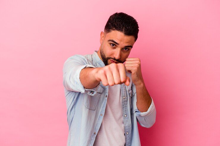 Foto jovem mestiço isolado em um fundo rosa dando um soco, raiva, lutando devido a uma discussão, boxe.