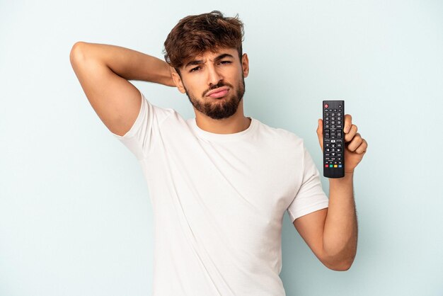 Jovem mestiço segurando um controlador de tv isolado em um fundo azul, sendo chocado, ela se lembrou de uma reunião importante.