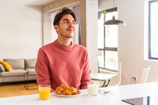 Jovem mestiço tomando café da manhã em uma cozinha sonhando em alcançar objetivos e propósitos