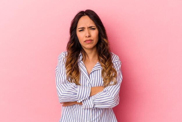 Jovem mexicana isolada em um fundo rosa suspeito, incerto, examinando você.