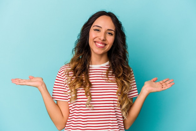 Jovem mexicana isolada na parede azul faz escala com os braços, sente-se feliz e confiante.