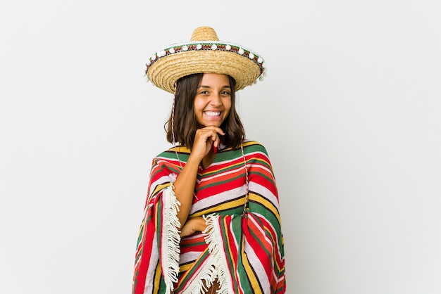 Jovem mexicana isolada na parede branca, sorrindo feliz e confiante, tocando o queixo com a mão.