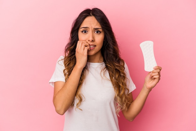 Foto jovem mexicana segurando uma compressa isolada em unhas rosadas roendo, nervosa e muito ansiosa.