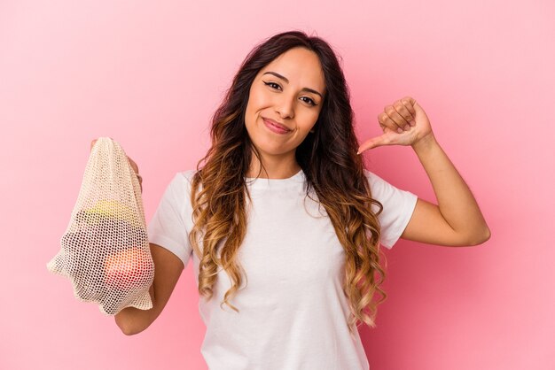 Jovem mexicana segurando uma sacola de frutas isolada em um fundo rosa sente-se orgulhosa e autoconfiante, exemplo a seguir.