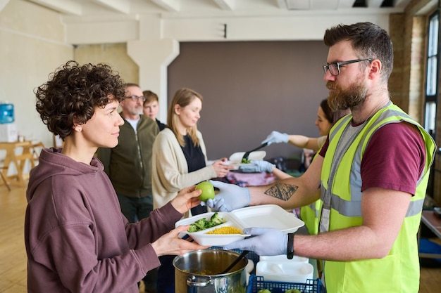 Jovem migrante séria levando recipiente com comida e olhando para o voluntário