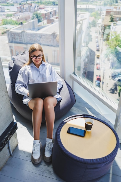 Jovem milenar em óculos de proteção ocular clássicos conectando-se à internet WIFI no laptop no espaço de coworking para navegar nas informações da web em netbooks digitais mulher europeia conversando