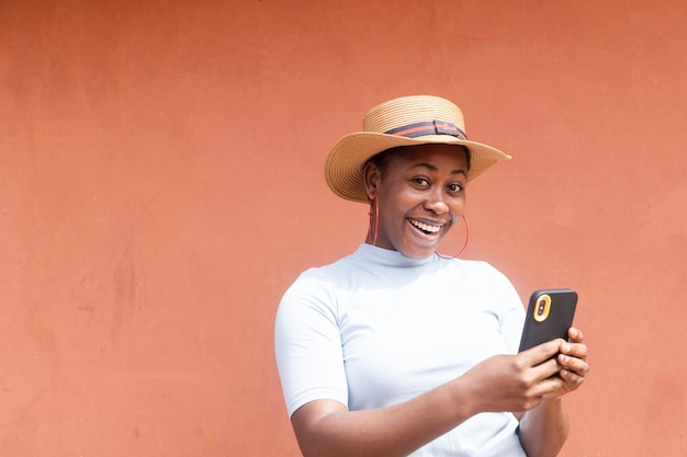 Jovem modelo africano negro sorrindo olhando para a câmera com o celular na mão