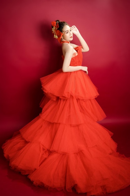Jovem modelo asiática de mulher bonita em um vestido vermelho de luxo elegante e elegante sobre um fundo vermelho isolado.