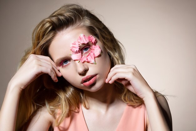 Jovem modelo atraente posando perto de uma parede de luz com pétalas de flores no rosto