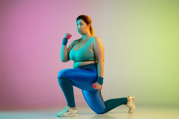 Jovem modelo feminino caucasiano plus size treinando na parede gradiente verde roxo