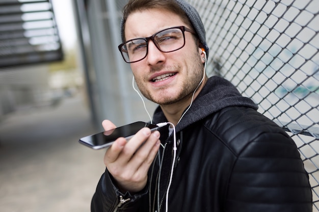 Jovem moderno falando ao telefone com as mãos livres na rua.
