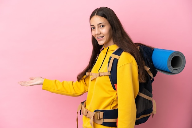 Jovem montanhista com uma grande mochila isolada em um fundo rosa estendendo as mãos para o lado para convidar a vir