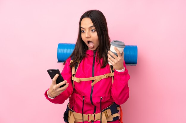 Jovem montanhista com uma grande mochila rosa segurando um café para levar e um celular