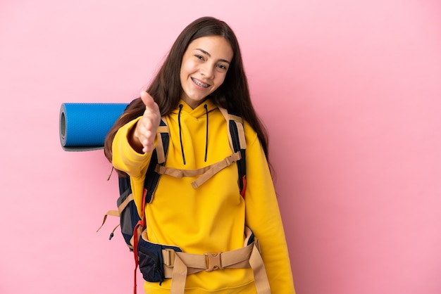 Jovem montanhista com uma mochila grande isolada em um fundo rosa apertando as mãos para fechar um bom negócio