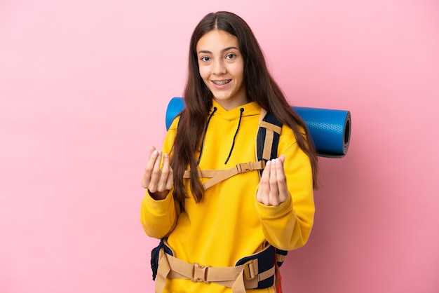 Jovem montanhista com uma mochila grande isolada em um fundo rosa fazendo gesto de dinheiro
