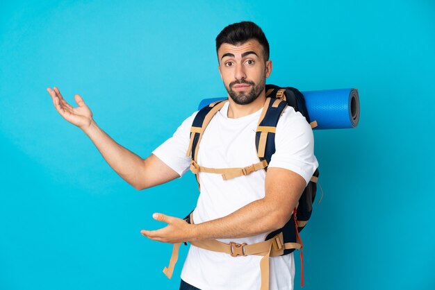 Jovem montanhista sobre uma parede azul isolada estendendo as mãos para o lado para convidar para vir