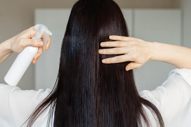 Jovem morena aplicando spray de cabelo no cabeloFeche