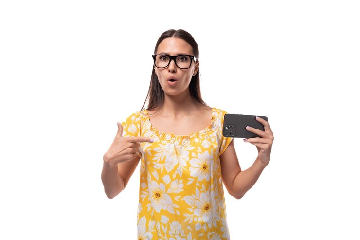 Foto jovem morena atraente aponta com surpresa para seu smartphone