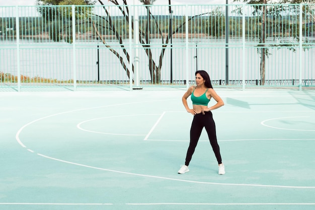 Foto jovem morena atraente fazendo exercícios e posando no campo de esportes ao ar livre