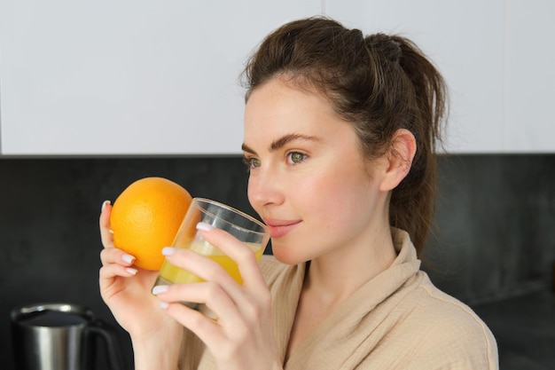 Jovem morena bebendo suco de laranja na cozinha moderna branca e uma garota sorridente segurando um copo de