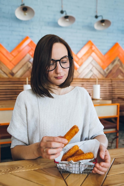 Foto jovem morena bonita come palitos de queijo frito de uma cesta de ferro decorada em um café. comida rápida. tonificação.