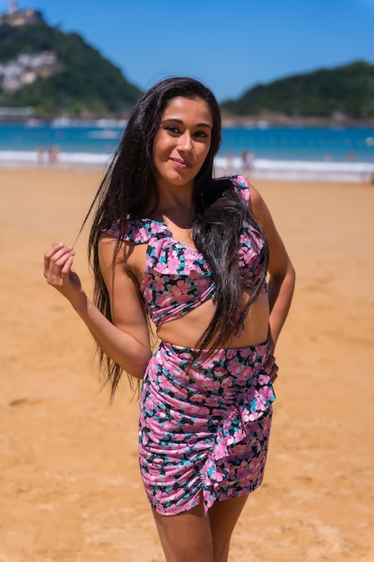 Jovem morena caucasiana curtindo o verão na praia de saia rosa sorrindo férias