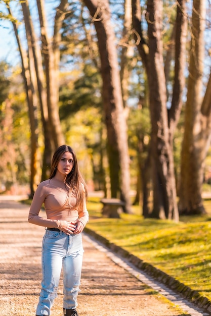 Jovem morena caucasiana em um suéter rosa e jeans andando em um parque no outono