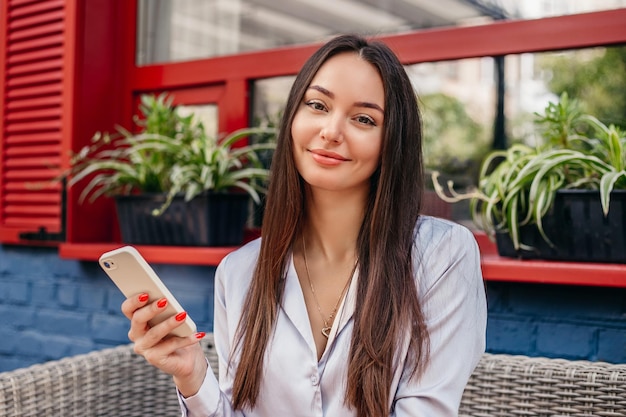 Jovem morena caucasiana usa seu smartphone enquanto está sentado em um café