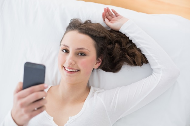 Jovem morena com celular na cama