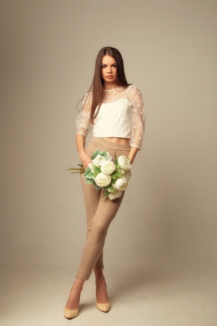 Foto jovem morena com flores posando e olhando para a frente sobre a superfície bege