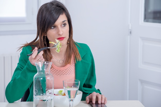 Jovem morena com jaqueta verde, comendo salada