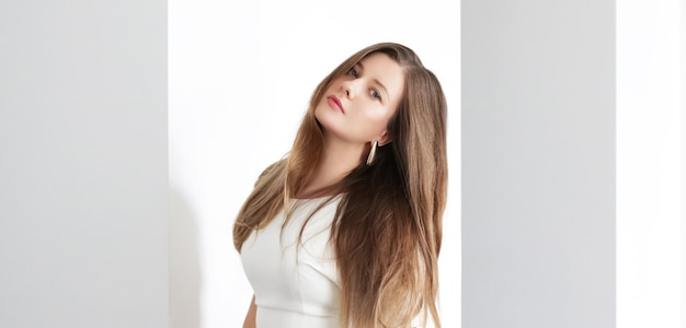 Jovem morena com penteado longo ondulado no interior branco, cuidados com os cabelos e conceito de beleza de luxo