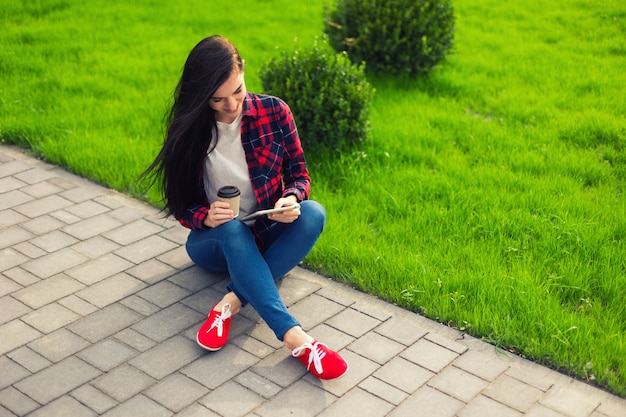 Jovem morena com tablet servindo na internet na grama