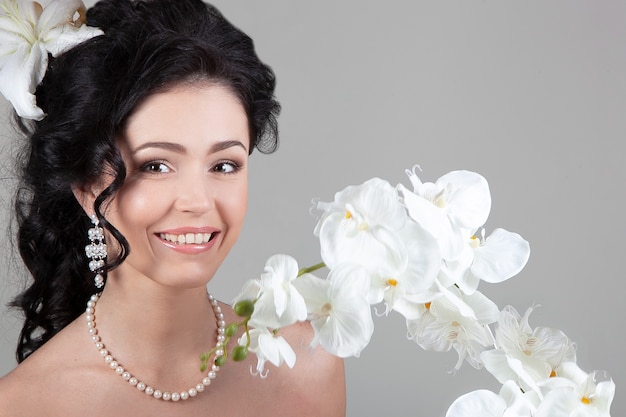 Jovem morena com um lindo penteado, colar de pérolas e brincos sorrindo cercada