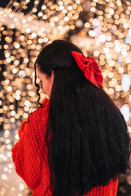 Jovem morena com um suéter tricotado de inverno e um laço vermelho no cabelo em uma atmosfera festiva