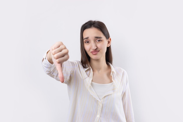 Jovem morena com uma blusa azul fazendo gesto com o polegar para baixo e olhando com expressão negativa