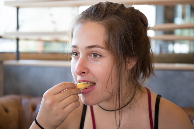 Jovem morena comer batatas fritas no restaurante hambúrguer