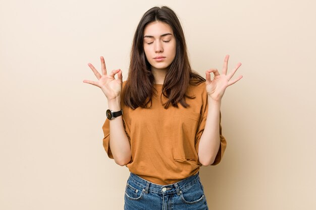 Foto jovem morena contra um bege relaxa após um duro dia de trabalho, ela está realizando ioga.