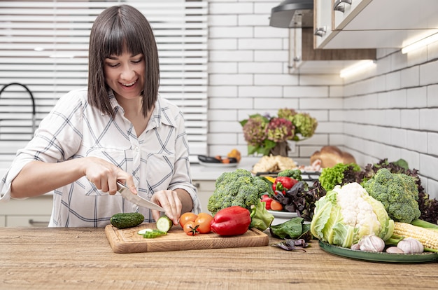 Jovem morena corta legumes na salada no espaço interior da cozinha moderna.